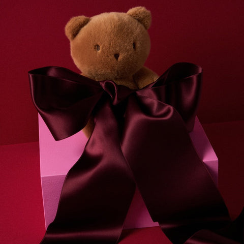 Brown teddy bear with a large purple bow on a red background